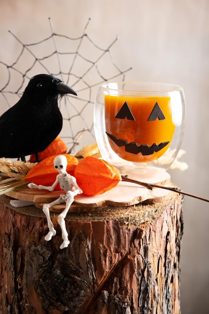 Pumpkin juice in a glass cup depicting Jack's pumpkin on a wooden stump next to a skeleton and a black crow Halloween Concept