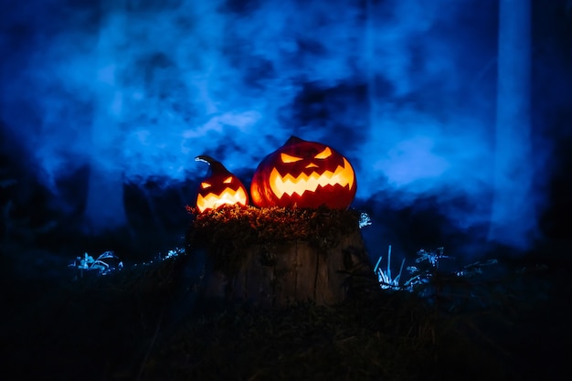 Pumpkin lanterns with jacks carved faces on the traditional horror festival in the forest with smoke