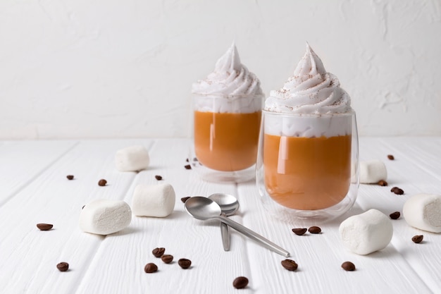 Pumpkin latte with whipped cream and spices on white wooden table.