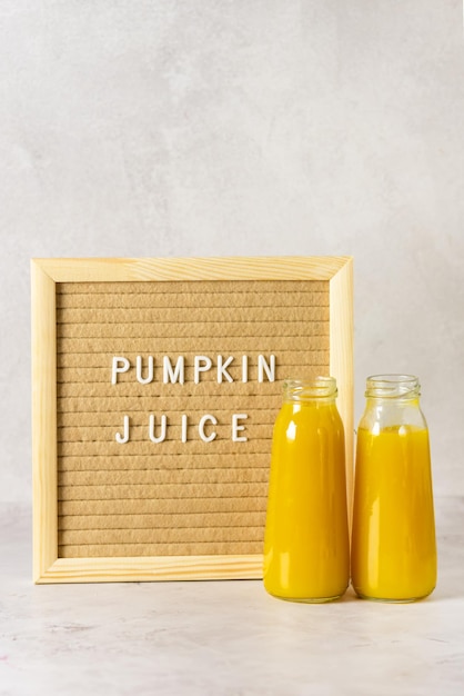 Pumpkin or Orange Cocktails or Juice in Bottle Board with Text Pumpkin Juice Gray Background