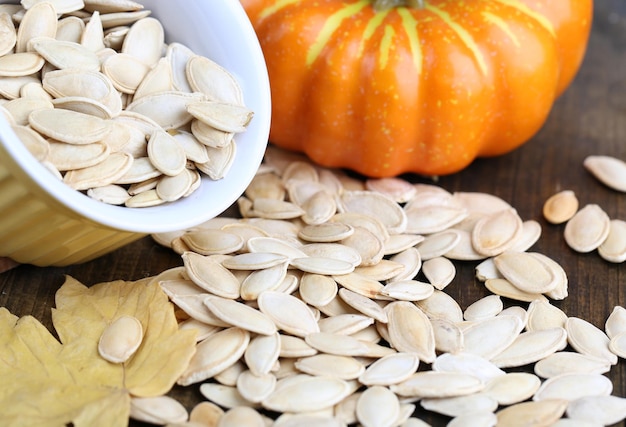 Pumpkin seeds in bowl with pumpkin on table close up