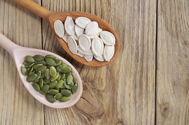 Pumpkin seeds green and unpeeled in the spoon on wooden background, top view