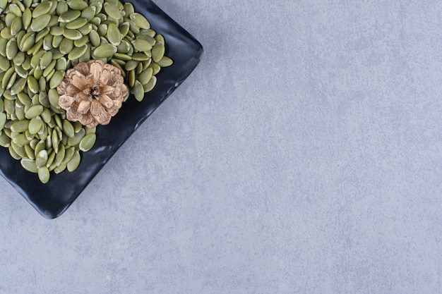 Pumpkin seeds and pine cone on a platter on the marble surface