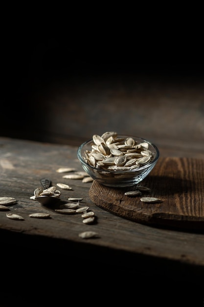 Pumpkin seeds in a transparent saucer on a wooden background