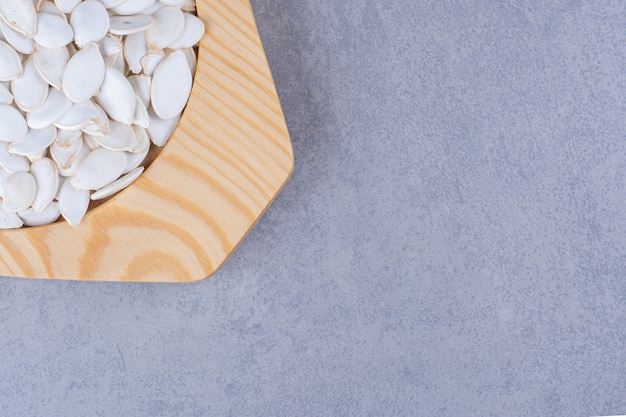 Pumpkin seeds in a wooden plate, on the marble.