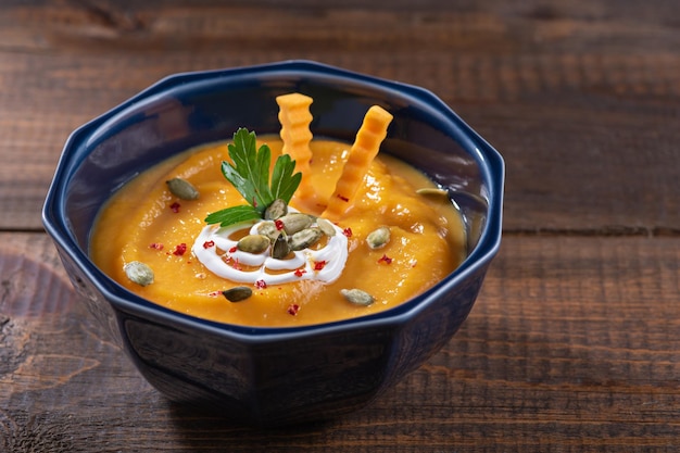 Pumpkin soup in blue plate on wooden table decorated with pumpkin seeds and parsley autumn seasonal recipes concept