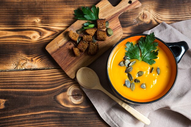 Pumpkin soup in a bowl with seeds and parsley on a wooden table