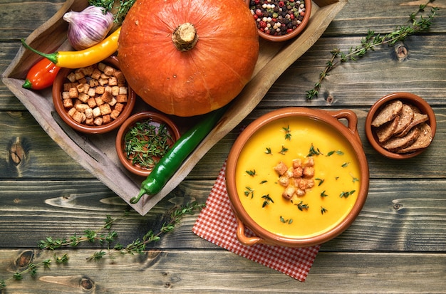 Pumpkin soup in ceramic bowl on rustic wood served with thyme and croutons, with  ingredients around