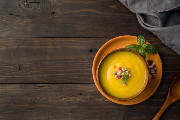 Pumpkin soup mashed with spices in wooden bowls on dark board background