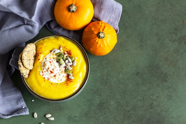 Pumpkin soup served in a bowl with cream, seeds and multigrain crackers.