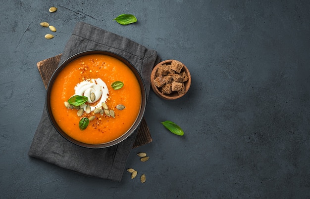 Pumpkin soup with cream and carrots on a dark gray background Top view copy space