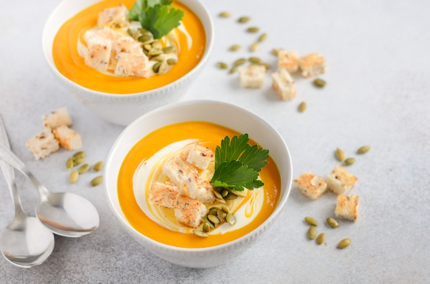 Pumpkin soup with cream, croutons, pumpkin seeds and parsley on a gray concrete or stone.