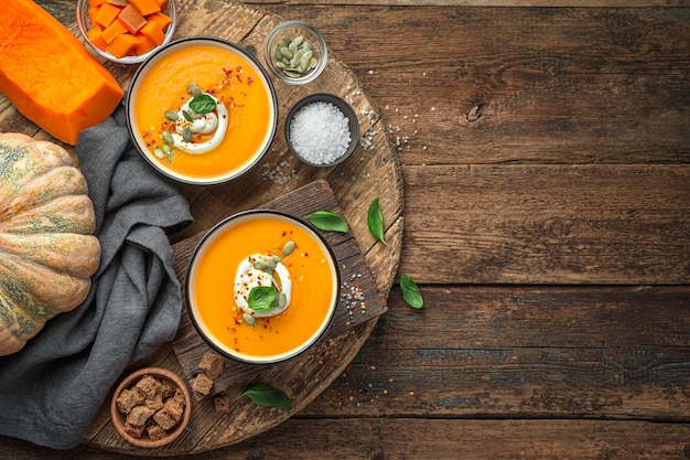 Pumpkin soup with cream spices and basil in two serving bowls on a natural wooden background