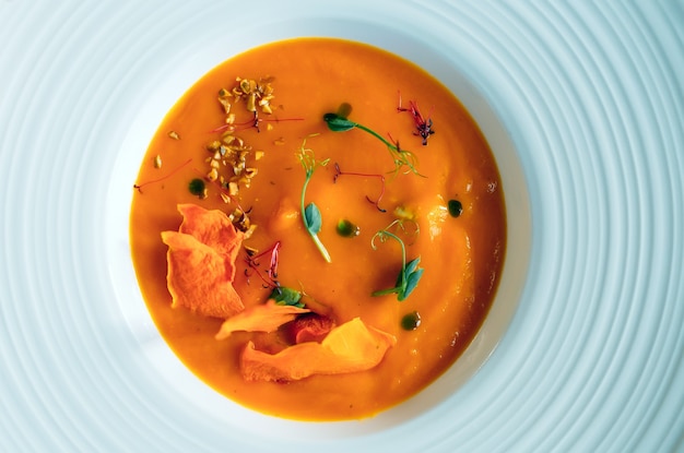 Pumpkin soup with greens on white plate