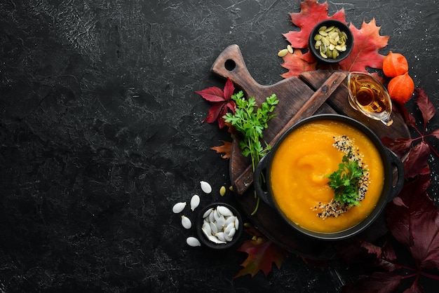 Pumpkin soup with pumpkin and colored autumn leaves flat lay On a black stone background Top view Free space for your text