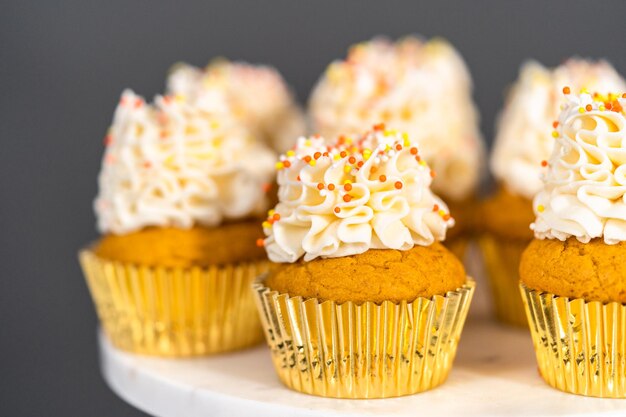 Pumpkin spice cupcake with Italian buttercream and sprinkles on a cake stand.