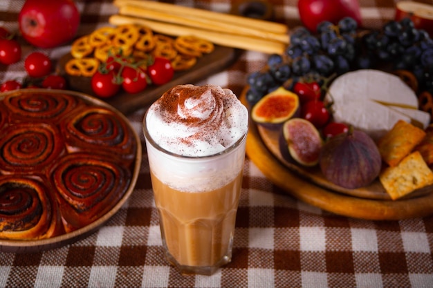 Pumpkin spice whipped latte in glass. Hot autumn drink beverage. Nearby delicious pie and appetizers fruits and cheese.