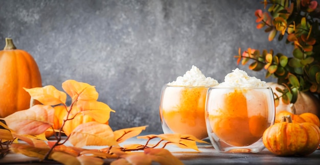 Pumpkin spiced latte or coffee in double glass cup on gray table Autumn or winter hot drink in festive orange table setting