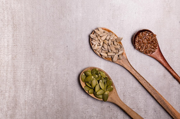 Pumpkin sunflower flax seeds on wooden spoons and oil in a glass vessel Closeup gray background