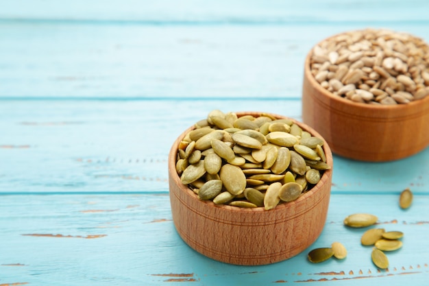 Pumpkin and sunflower seeds in bowl on blue wooden background. Top view