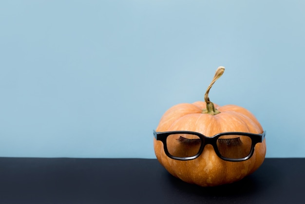 Pumpkin with false eyelashes and sunglasses on blue background, Halloween