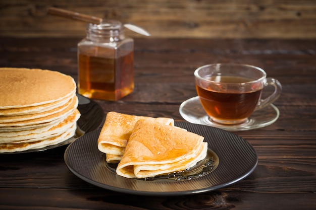 Puncakes with honey and cup of tea on old wooden surface