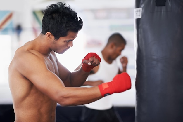 Punching bag man and boxing fitness with at a gym for training resilience or performance training Sports body and male boxer profile with punch practice for strength energy for fighting exercise