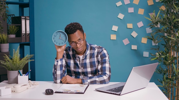 Punctual man checking time on wall clock and feeling upset about work delay, showing hour and minutes. Unhappy adult feeling displeased about running late to office job, deadline timing.