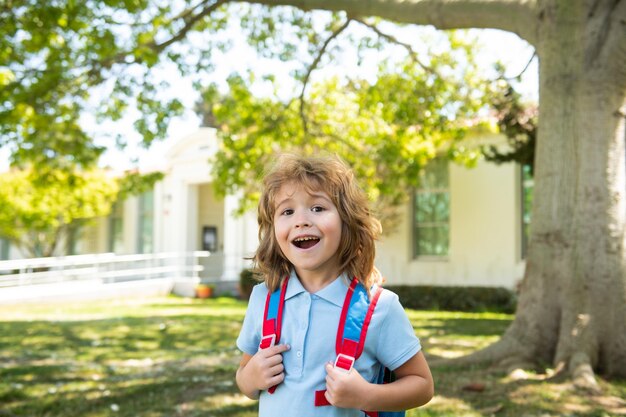 Pupil of primary school with book in hand near school park schoolboy with backpack near building out