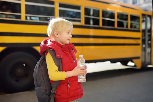 Pupil with schoolbag and bottle of water near yellow school bus 