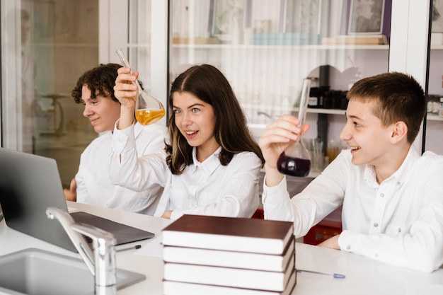 Pupils holding flasks with liquid for experiments in laboratory Education concept Group of pupils studying chemistry lesson in school