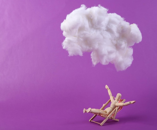 Puppet sunbathing on deck chair with cloud on purple background Creative idea Summer beach rest Minimal concept