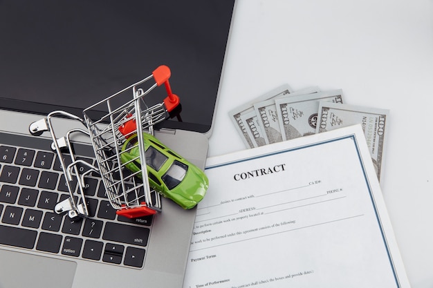 Purchase contract for a car with laptop, money and toy car in a shopping cart.