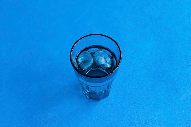 Pure drinking water with ice in a transparent blue glass on blue