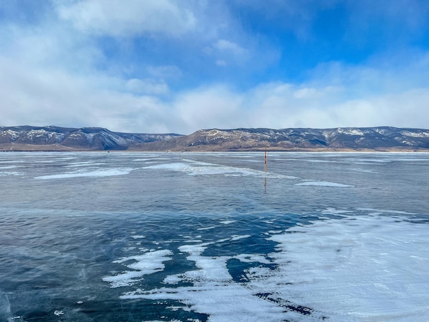 Pure ice of the frozen lake Baikal against the background of mountains frozen winter Baikal