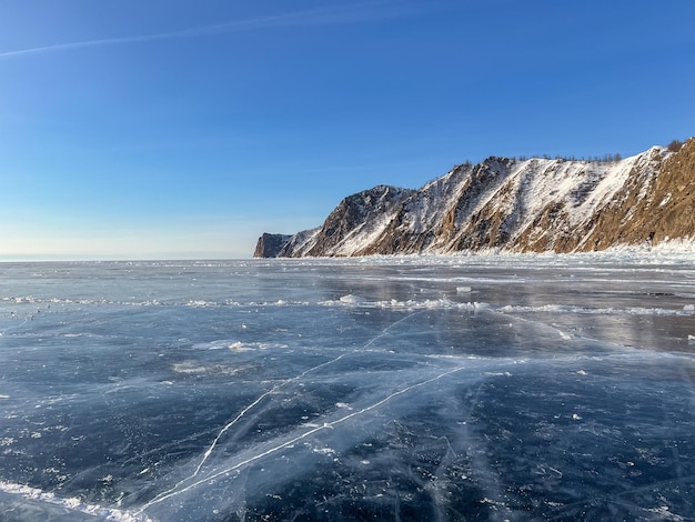 Pure ice of the frozen lake Baikal against the background of mountains frozen winter Baikal