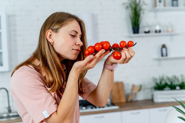 Pure, ripe juicy tomatoes in the woman's hands of a kitchen background. Table full of vegetables and fruits, modern kitchen