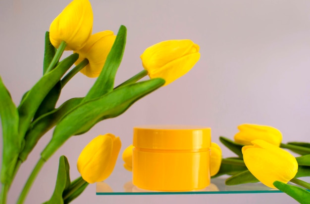 A pure yellow cosmetic container with a bouquet of tulips on a pink background. Empty packaging with labels for the brand layout. The concept of spring natural cosmetics, a banner of a cosmetic sale.