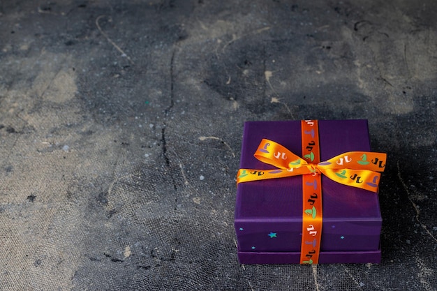 Purple box tied with orange ribbon with halloween drawings on dark background copy space