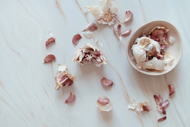 purple garlic cloves opened on a marble table and bowl with parts of garlic