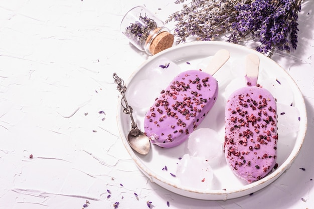 Purple Lavender flavored ice cream. Flower bouquet, vintage silver spoon, ceramic stand. Modern hard light, dark shadow. White putty background, copy space