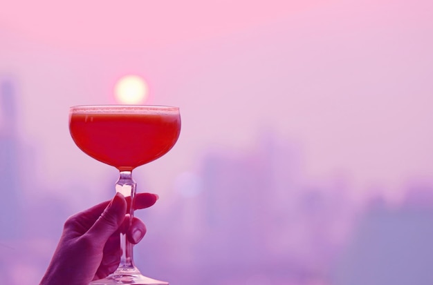 Purple and red colored cocktail glass in hand with blurry city aerial view in the backdrop