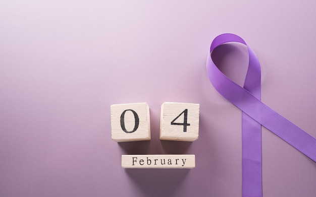 Purple ribbon and wooden calendar on pastel paper background for supporting World Cancer Day campaign on February 4