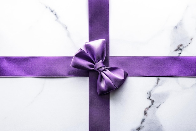 Purple silk ribbon and bow on luxury marble background holiday flatlay backdrop