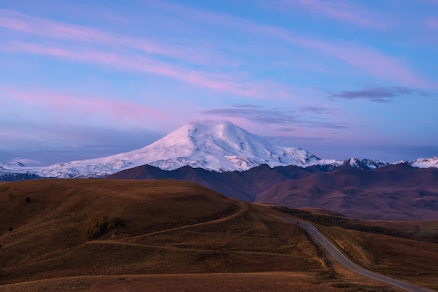 Purple twilight with snowcapped mountain top and highway through autumn valley