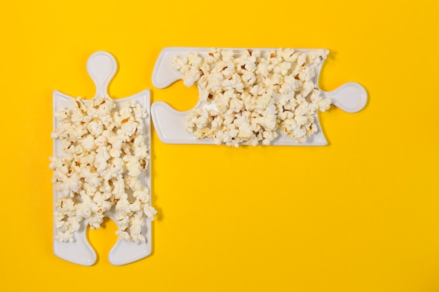 Puzzle dishes with popcorn on a yellow background. The best company to watch a movie