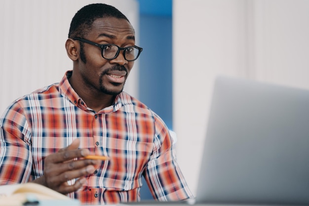 Puzzled african american employee in glasses looking at laptop screen shocked by problems in work