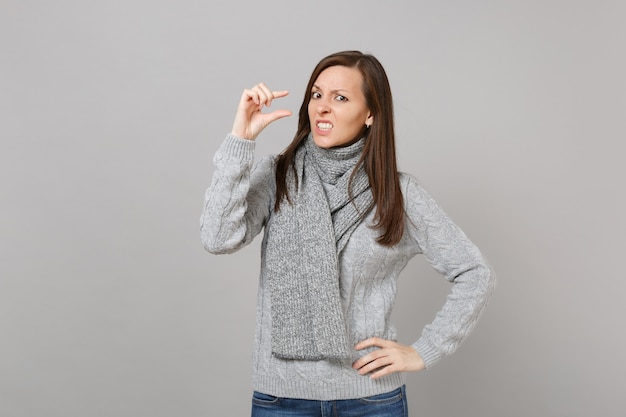 Puzzled woman in gray sweater scarf gesturing demonstrating size with copy space isolated on grey background. Healthy fashion lifestyle people sincere emotions cold season concept. Mock up copy space.