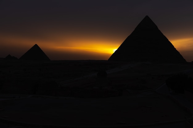 Photo the pyramids at sunset, silhouettes in the dark in giza, egypt.