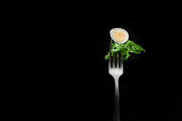 Quail egg with salad on a fork on a black background isolated